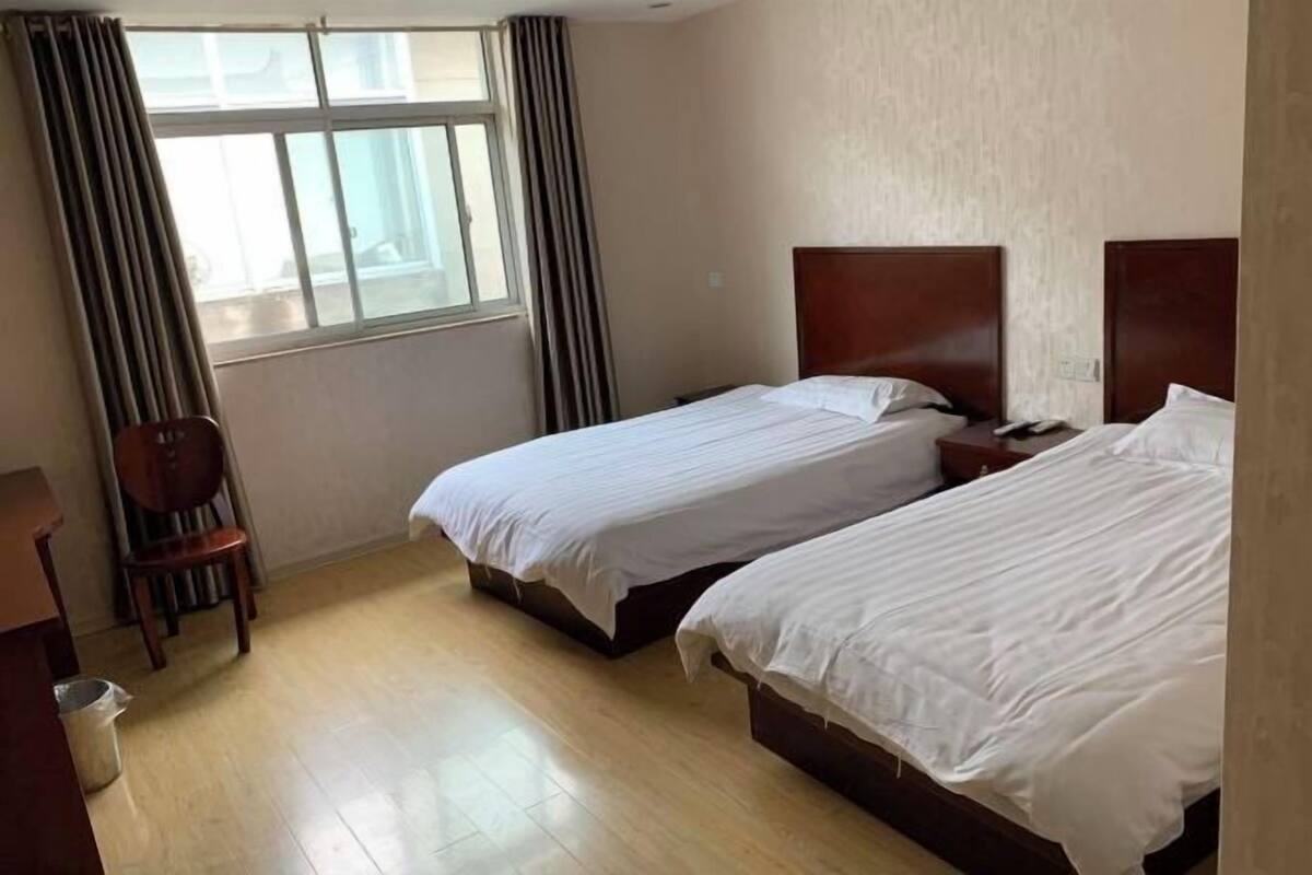 A hotel room with two single beds, a wooden chair, a desk, and a window with curtains.