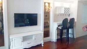 A room with a flat-screen TV mounted on a white cabinet, a small white table, and two black chairs. - YangZhou FuRun Hotel (Yangzhou)