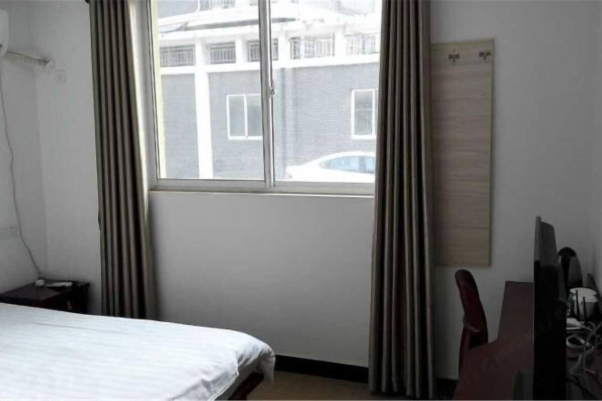 A hotel room with a bed, a desk, a chair, a window with curtains, and a wall-mounted TV.