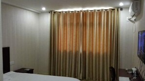 A hotel room with a bed, a desk with a computer, a chair, and a curtain. - YangZhou FuRun Hotel (Yangzhou)