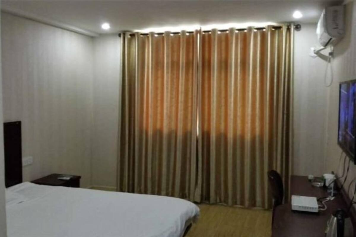 A hotel room with a bed, a desk with a computer, a chair, and a curtain.