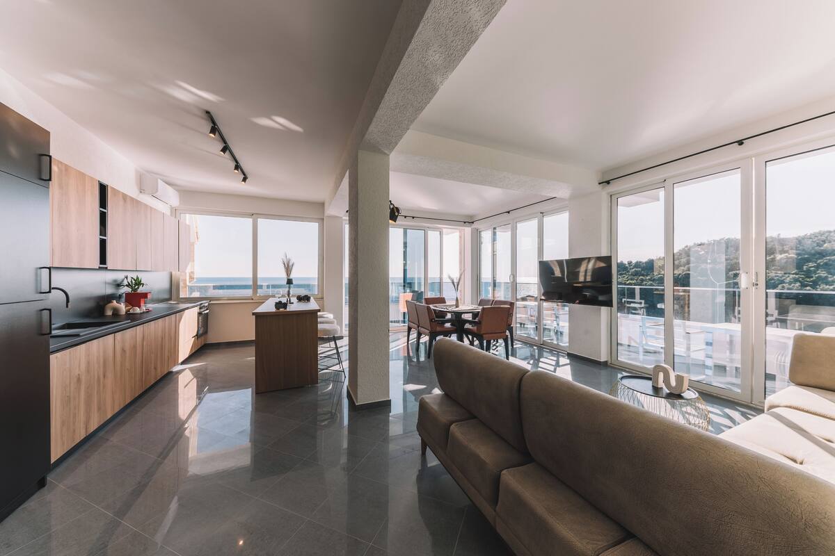 A modern apartment with a kitchen, dining area, and living room, featuring large windows and a view of the city.