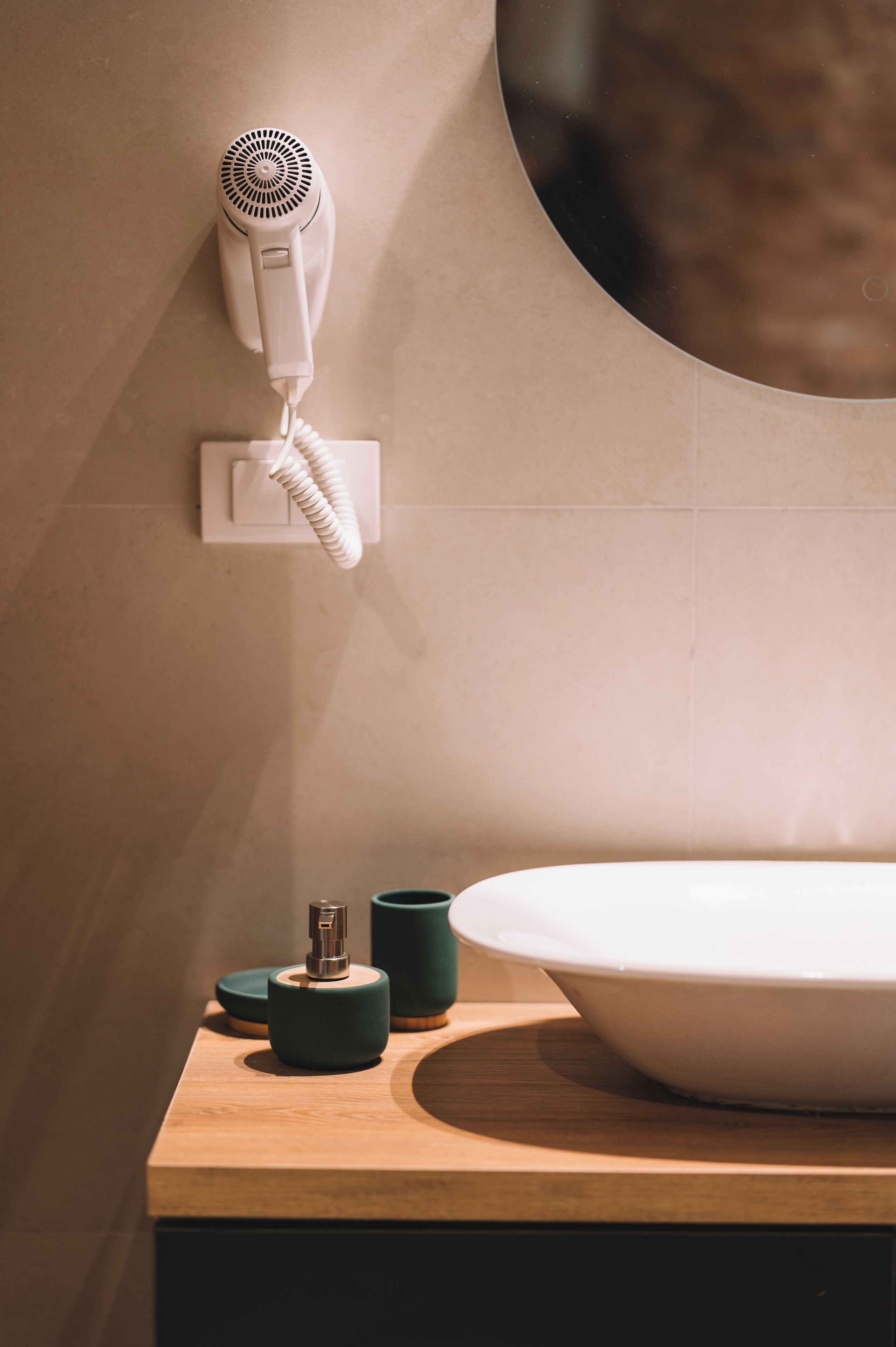 A bathroom with a large white sink, a hairdryer mounted on the wall, and two small teal containers on the counter.
