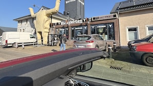 A W.O.A. Wacken store with a large statue in front, parked cars, and a clear blue sky.