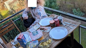 A person sitting at an outdoor table with breakfast items, including eggs, biscuits, and milk.