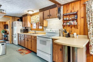 Compact kitchen with a stove, refrigerator, and sink, featuring exposed wooden beams and a patterned rug.