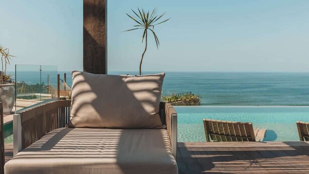 A sunlit lounge area with a view of the ocean, a palm tree, and a pool. - Marina at Caivama (Sayulita)