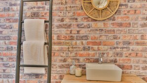 A bathroom with a brick wall, a white sink, a wooden vanity, a towel rack, and a decorative basket.