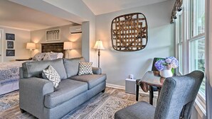 Un salon moderne avec un canapé gris, un fauteuil assorti et une petite table sur laquelle est posé un vase de fleurs. On peut également apercevoir un grand élément décoratif mural et une lampe.