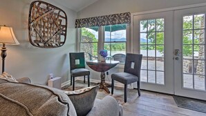 Une pièce avec une grande fenêtre, un élément décoratif mural, deux chaises, une table avec un vase et une lampe.