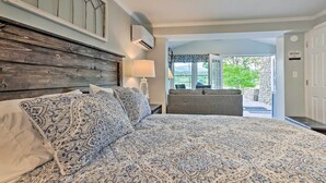 Une chambre à coucher avec un grand lit, une tête de lit en bois, une table de chevet avec une lampe, et une vue sur l’extérieur.