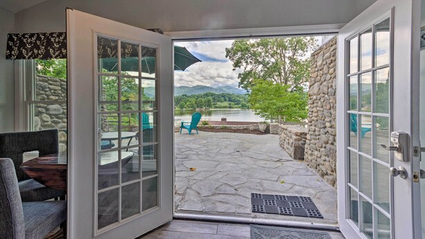 Vue depuis une pièce dont la porte est en verre et qui donne sur un patio extérieur avec un sol en pierre, une table et des chaises.