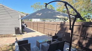 Una zona patio con mobili da esterno, un pergolato e vista su un giardino recintato in legno.