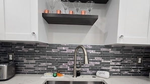 Una cucina con lavello in acciaio inossidabile, un tostapane e una parete rivestita di piastrelle.