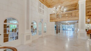 A spacious hotel lobby with a high ceiling, large arched windows, and a wooden balcony.