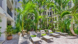 A courtyard with lounge chairs, a table, and potted plants. - Palm Beach Regency Walk to Beach (Palm Beach)