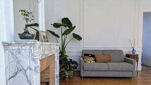 A living room with a marble fireplace, a grey sofa, and various potted plants. - Charming T2 with balcony in Lille-Centre (Lille)