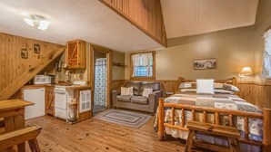 Una habitación acogedora de estilo cabaña con suelo de madera, una cama con colcha, un sofá, una mesita y una kitchenette con microondas y refrigerador.