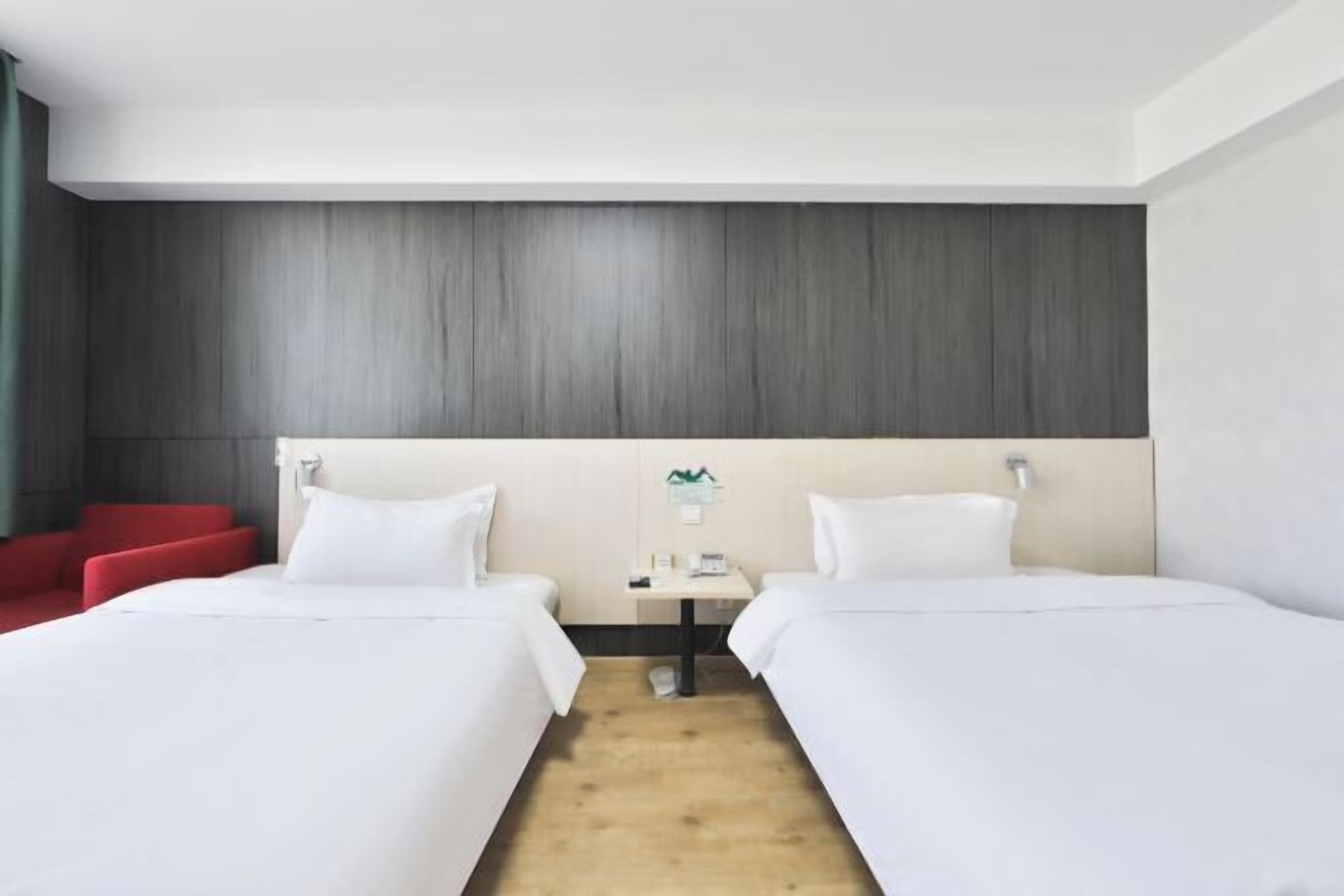 Hotellihuone, jossa on kaksi sänkyä, pieni pöytä, punainen tuoli ja puulattia.