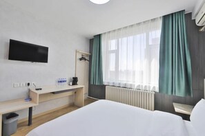 A hotel room with a bed, a desk, a TV, a radiator, and a window with curtains. - Wenna Hotel (Changchun Qianjin Street Qianwei Hospital) (Changchun)
