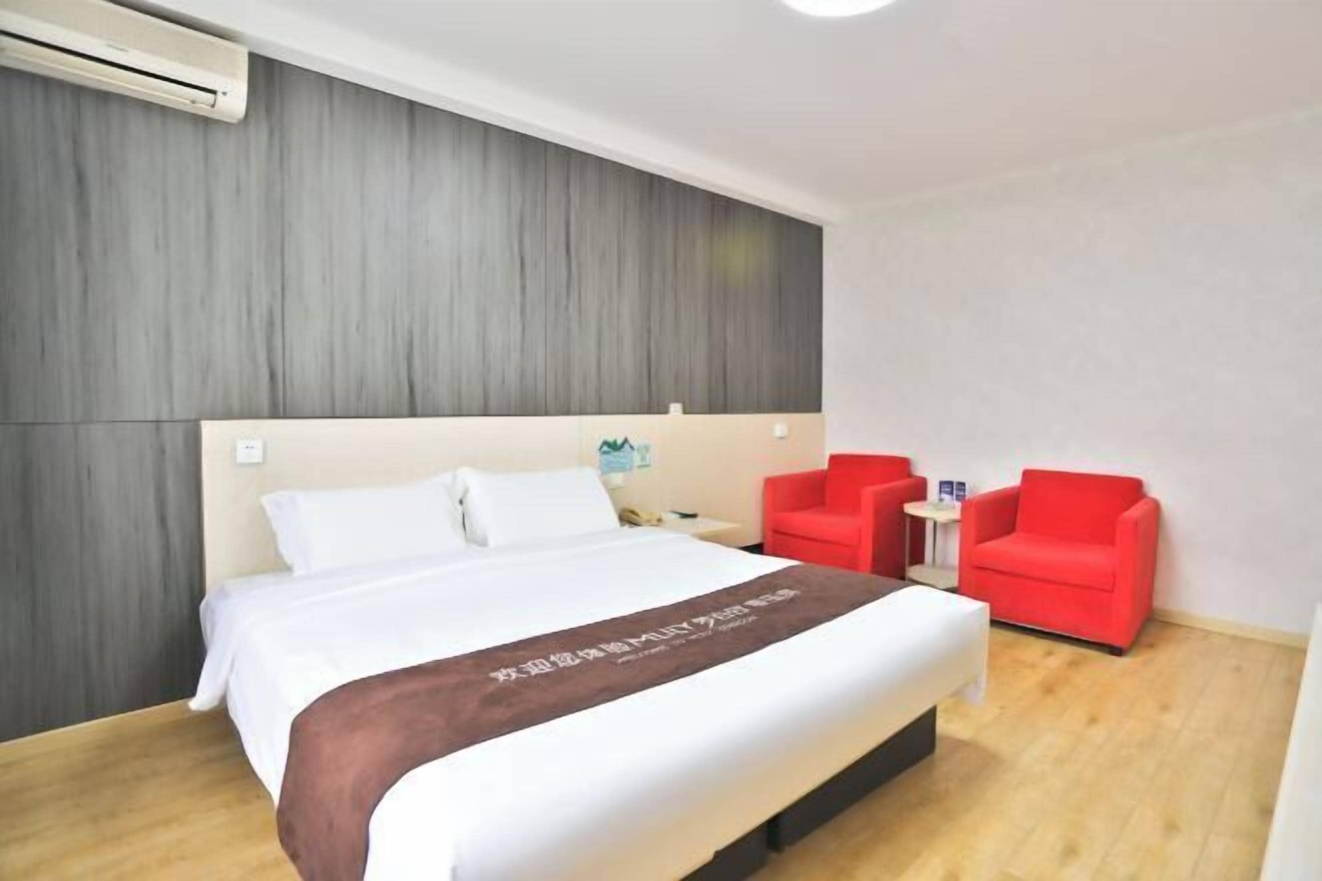 Une chambre d’hôtel avec un lit, une table de chevet, un fauteuil rouge, une petite table et un climatiseur fixé au mur.
