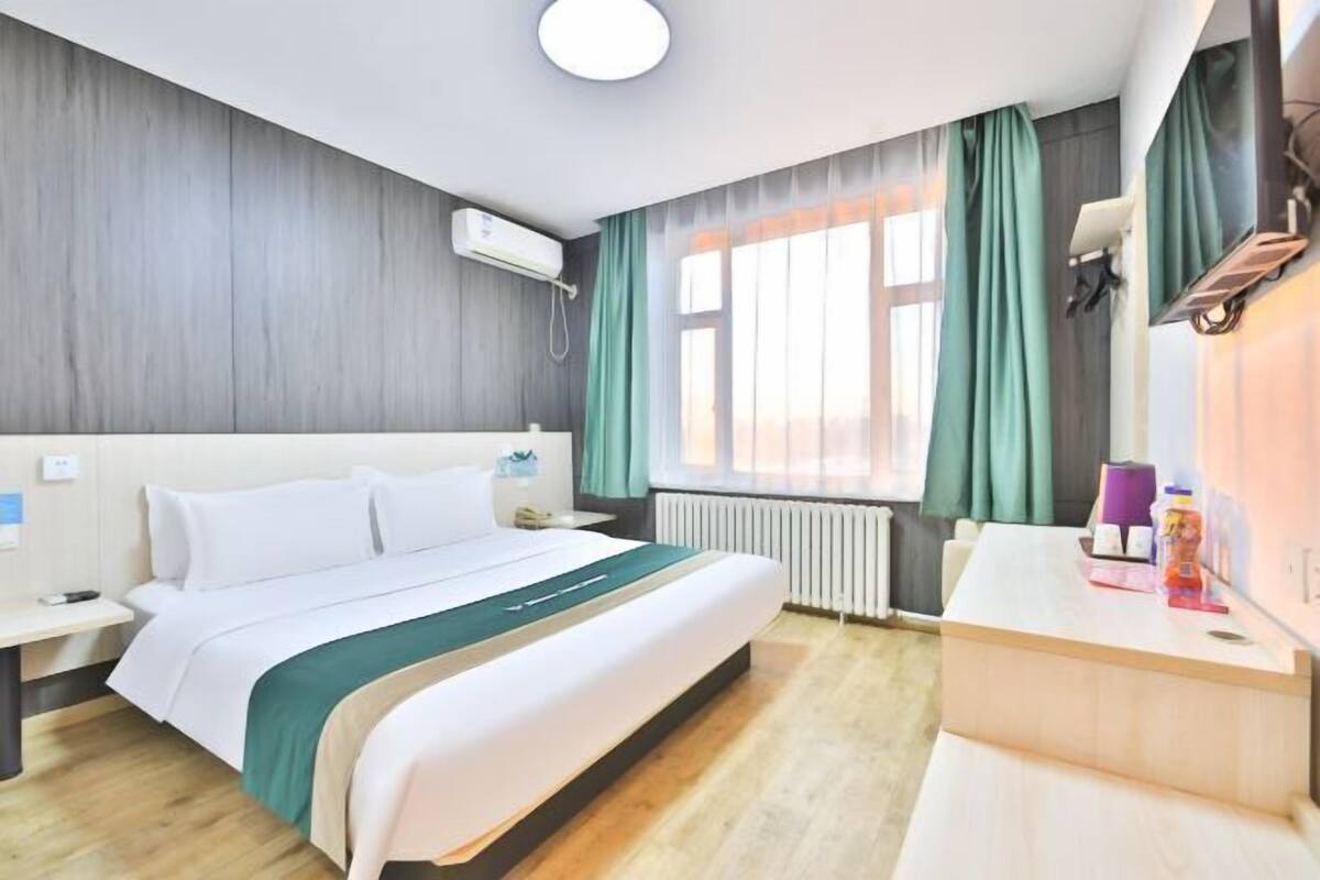 A hotel room with a bed, bedside table, and a desk with a chair.