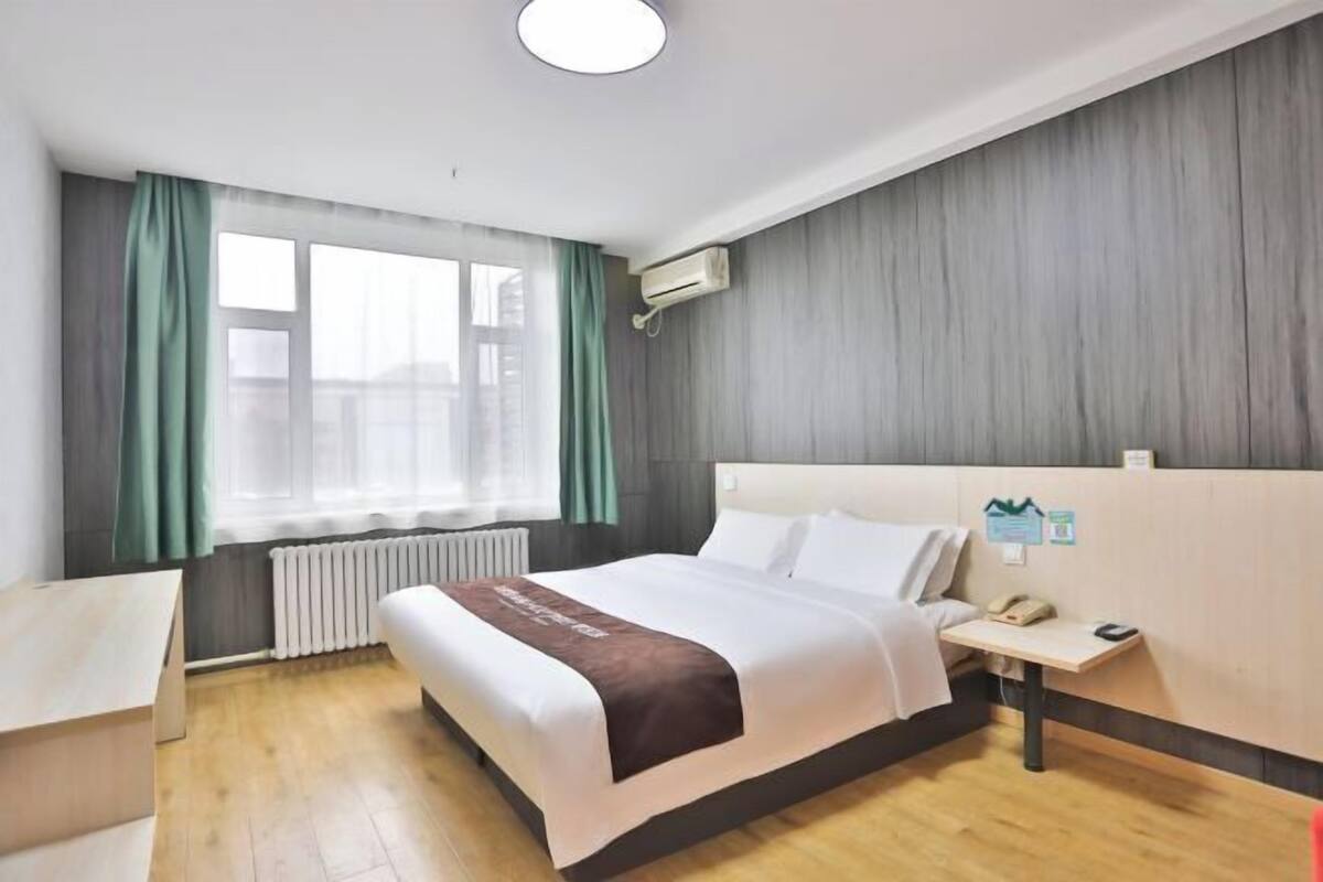 A hotel room with a bed, bedside table, and a window with curtains.