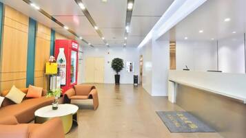 A reception area with a reception desk, seating area with sofas, a potted plant, and a wall-mounted refrigerator.