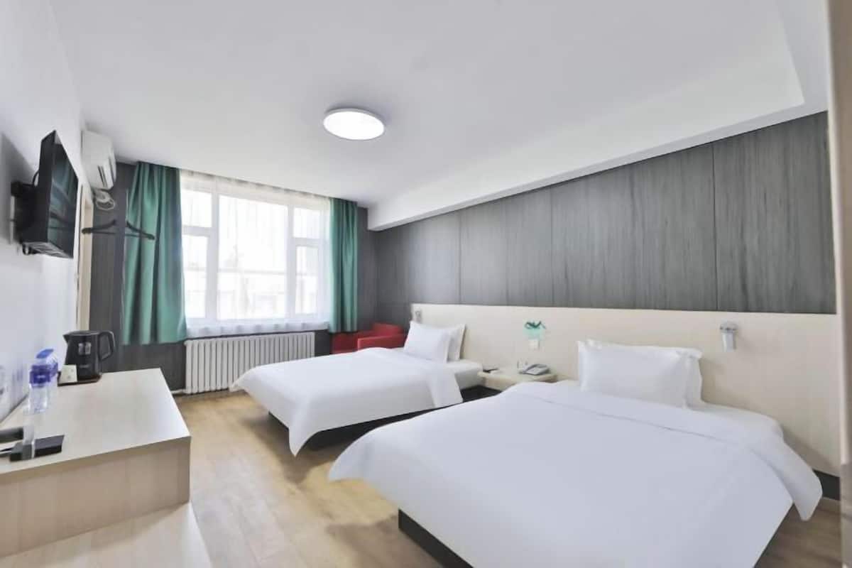 A hotel room with two beds, a desk, a TV, and a window with curtains.