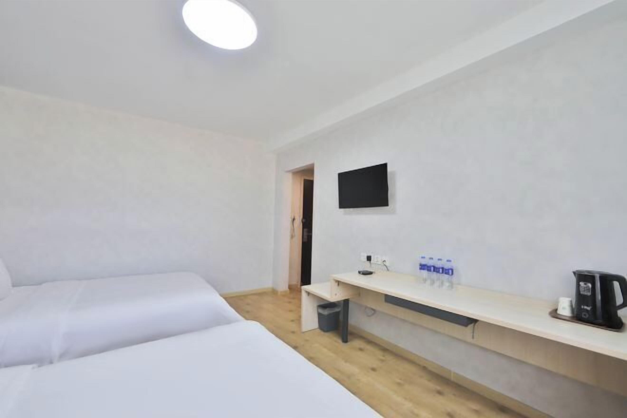 A hotel room with two beds, a desk with a flat-screen TV, a coffee maker, and a water dispenser.