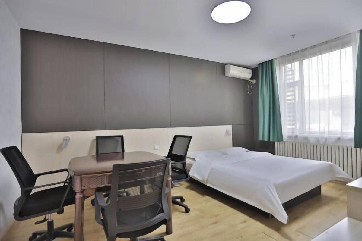 A hotel room with a bed, two chairs, a desk with a computer, and a window with curtains.