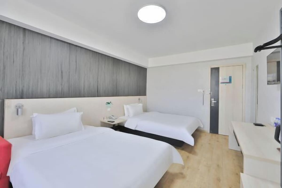 A hotel room with two beds, a desk, a chair, and a wardrobe.