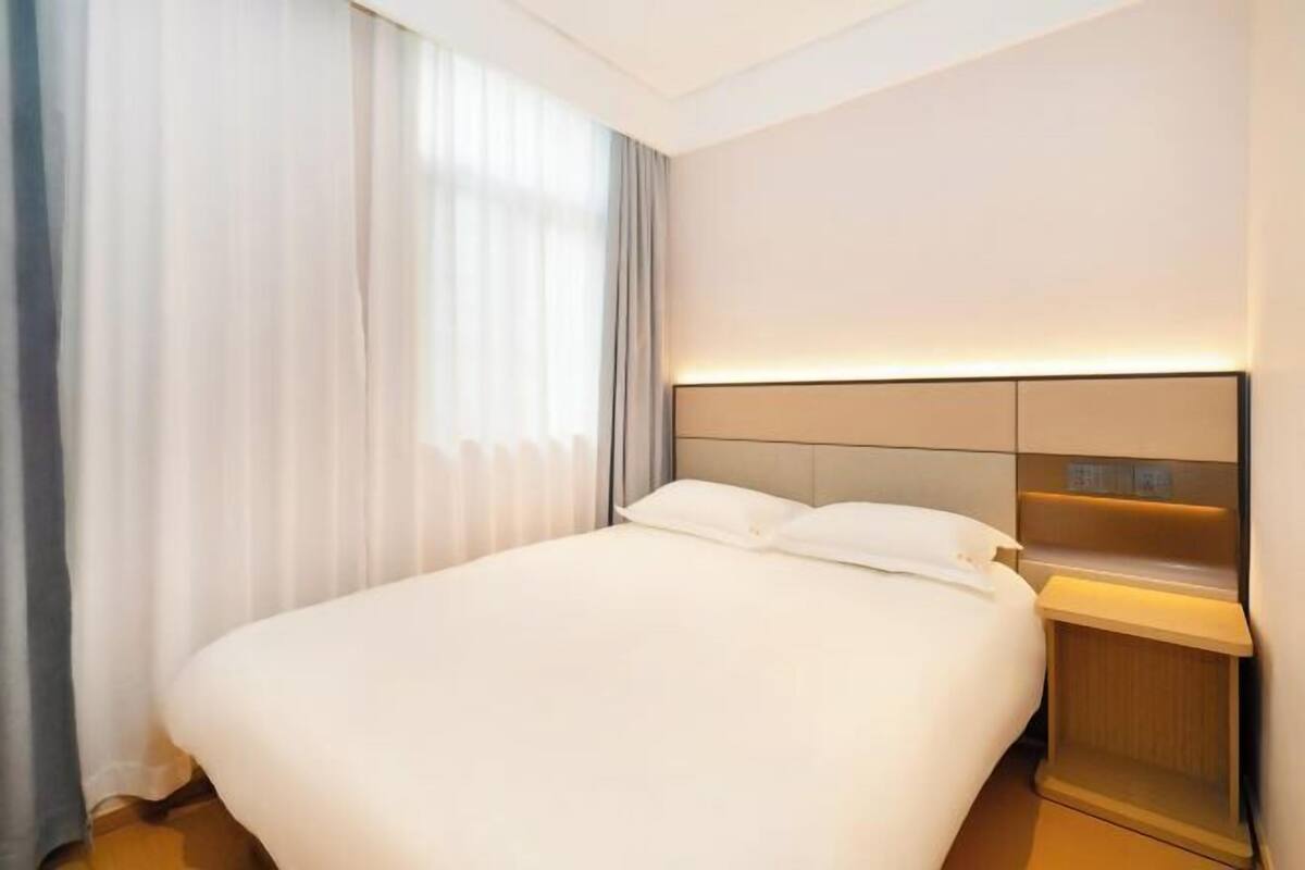 Une chambre d’hôtel avec un lit, des rideaux, une table de chevet et une lampe fixée au mur.