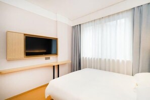 Ein Hotelzimmer mit Bett, Wandfernseher und einem fensterbepflanzten Fenster.