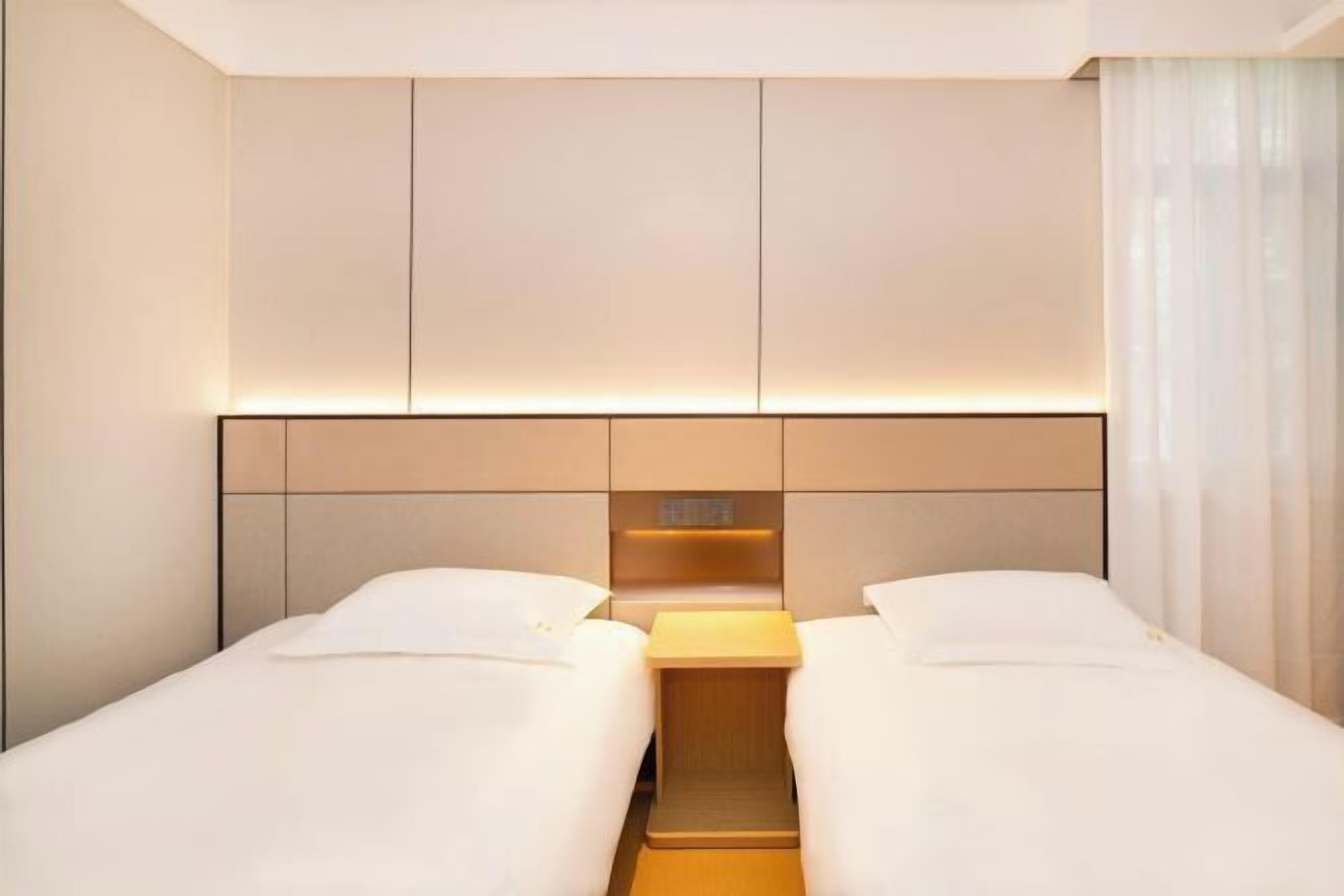 A hotel room with two beds, a wooden headboard, and a nightstand.
