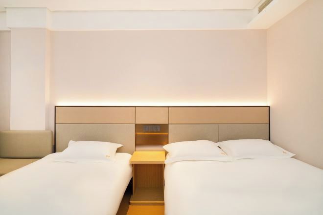 A hotel room with two beds, a nightstand, and a built-in shelf.