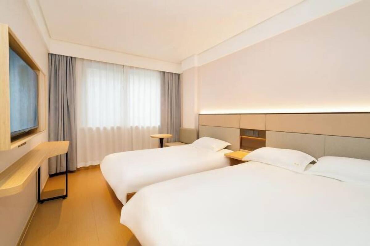 Une chambre d’hôtel avec deux lits, une télévision, une table de chevet et une fenêtre avec des rideaux.