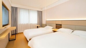 Une chambre d’hôtel avec deux lits, une télévision, une table de chevet et une fenêtre avec des rideaux.