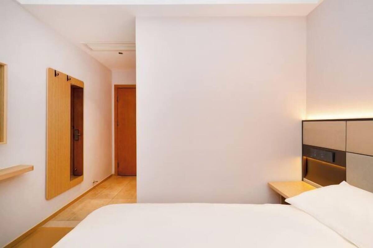 Une chambre d’hôtel avec un lit, une table de chevet, une commode et un miroir.