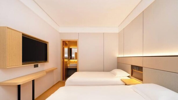 Una habitación de hotel moderna con cama, mesita de noche, televisión y vestidor.