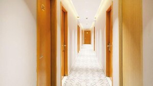 Un pasillo de hotel con puertas de madera, suelo estampado y una cálida luz en el techo.