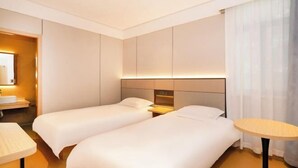 Une chambre d’hôtel avec deux lits, une table de chevet, une table ronde et une salle de bain équipée d’un lavabo et d’un miroir.
