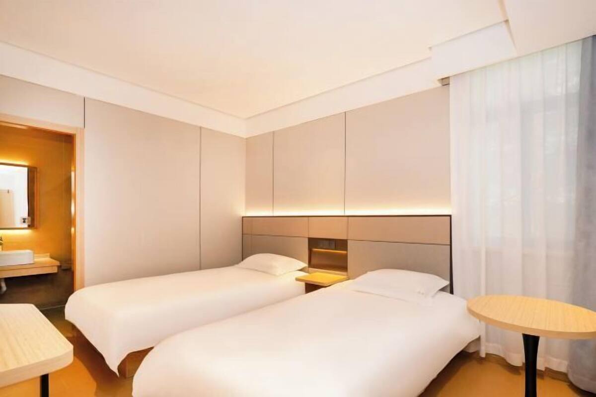Une chambre d’hôtel avec deux lits, une table de chevet, une table ronde et une salle de bain équipée d’un lavabo et d’un miroir.