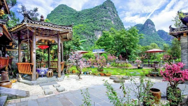 A traditional wooden pavilion with a tiled roof, surrounded by lush greenery and potted plants.