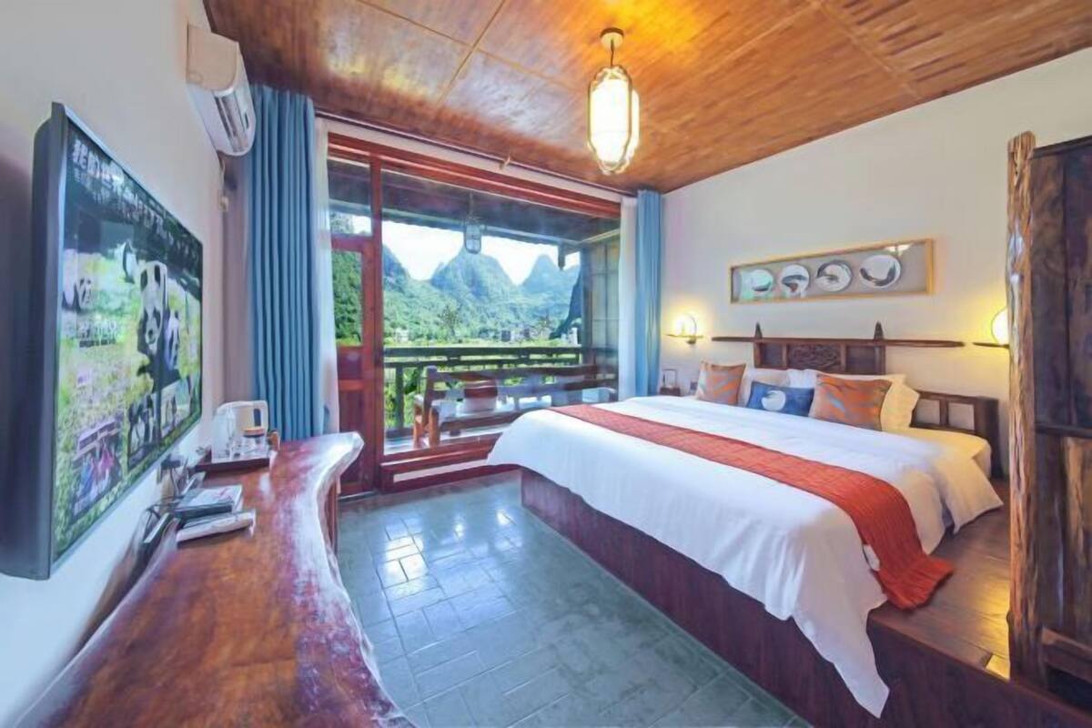 Een hotelkamer met een bed, een bureau met een computer, een raam met uitzicht op bergen en een houten plafond.