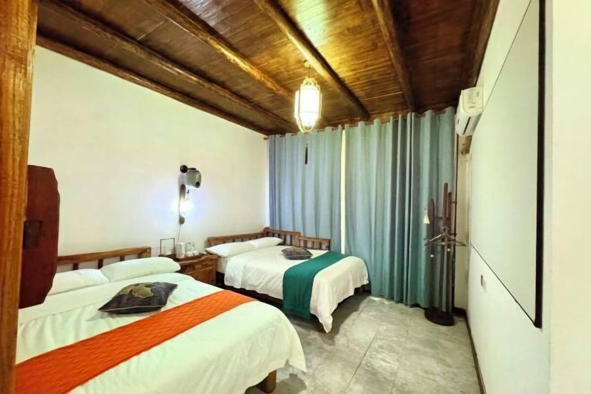 Een hotelkamer met twee bedden, houten balken in het plafond, een wandlamp en een gordijn.