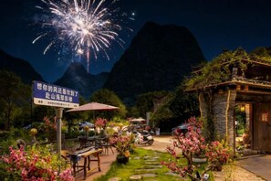 A restaurant with outdoor seating, surrounded by mountains and a night sky with fireworks.