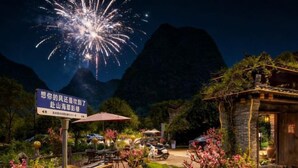 A restaurant with outdoor seating, a mountain backdrop, and a sign in a foreign language.