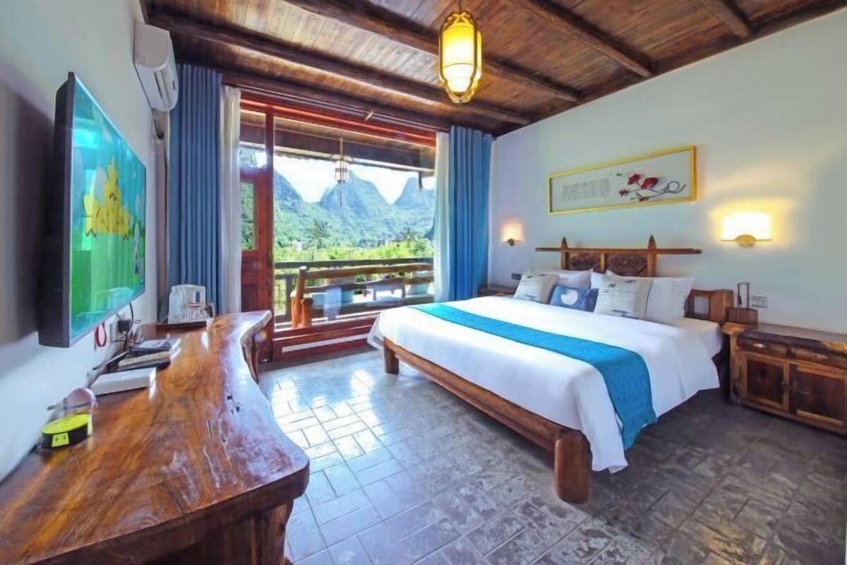 Een slaapkamer met een bed, een bureau, een stoel, een raam met uitzicht op bergen, en een plafondventilator.