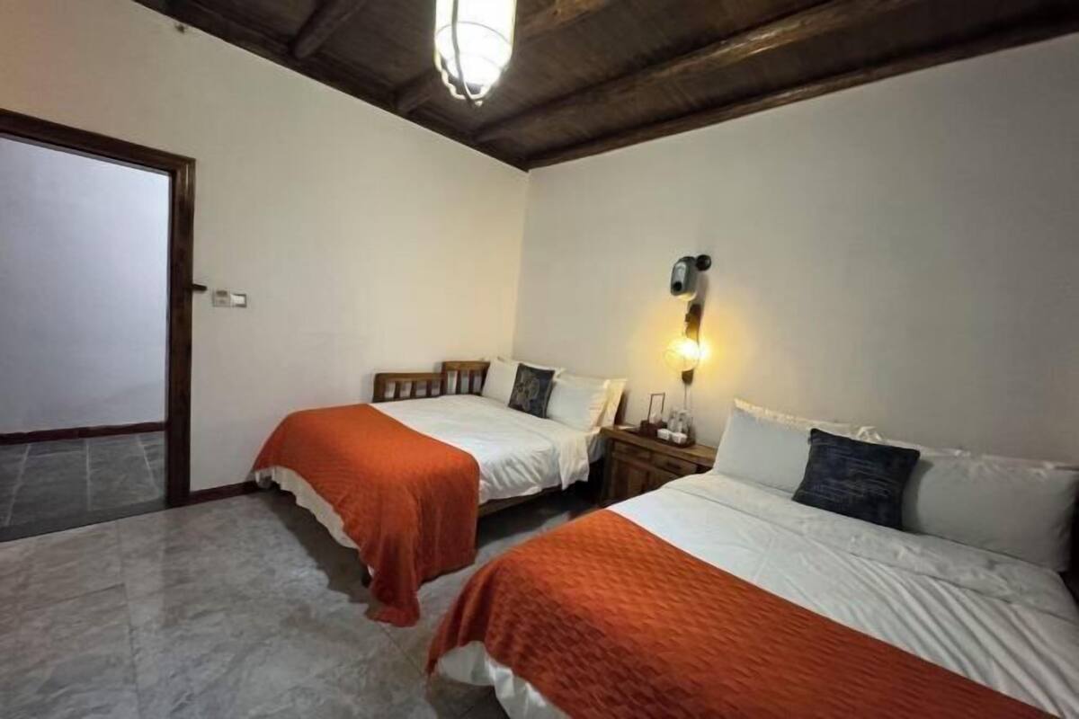 Een kamer met twee bedden, een houten plafond, een wandlamp en een deur.